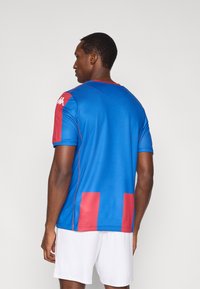 Αθλητική φανέλα Kappa, κοντομάνικη, μπλε με κόκκινες λεπτομέρειες, κατασκευασμένη από ελαφρύ ύφασμα, διαθέτει λογότυπο στον ώμο και σχέδιο με μοτίβο στην πλάτη.