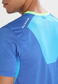 Camiseta deportiva azul con una superficie texturizada, que presenta detalles en azul claro y verde en los hombros y el escote, y la marca "DARE2B".