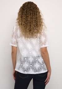 Top in pizzo bianco con maniche corte, caratterizzato da un motivo floreale, con una sfumatura dal bianco al nero sull'orlo, realizzato in un materiale leggero e con texture.