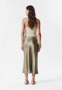 Beige Smocked-Top ohne Träger, kombiniert mit einem metallisch olivgrünen Satinrock, der ein fließendes Design und einen eleganten Look aufweist.