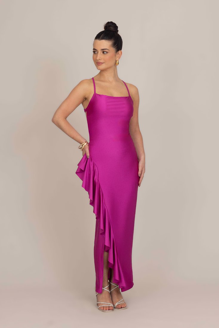 Prilagođena haljina bez rukava u vibrantnoj magenta satenskoj tkanini, sa volanom duž strane i elegantnim krojem do poda.