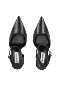 Zapatos de charol negros de punta con apertura en el talón, que cuentan con un diseño de corte curvado y una correa de tobillo con hebilla plateada.