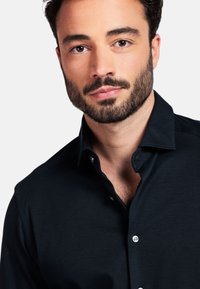 Zwarte overhemd met korte kraag, gemaakt van zacht stof. Heeft een gladde textuur en een nauwsluitende pasvorm rond de hals en schouders.