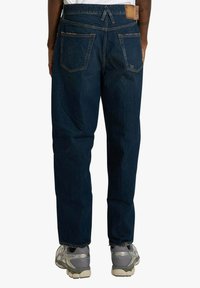 Jeans in denim blu scuro con vestibilità rilassata, caratterizzati da cinque tasche, cuciture visibili e toppa in pelle sulla cintura.