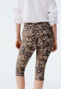 Legginsy o długości do połowy łydki w panterkowy deseń, wykonane z elastycznego materiału, o dopasowanym kroju, z paskiem w talii i tylnymi kieszeniami. Widok od tyłu pokazuje zakończenie nogawek tuż poniżej kolan.