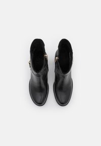 Zwarte leren enkellaarzen met een gladde textuur en afgeronde neuzen. Voorzien van goudkleurige ritsen aan de zijkanten. Eenvoudig, strak ontwerp.