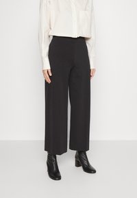 Zwarte wijde broek in een gladde stof, met een hoge taille en een getailleerde pasvorm, gecombineerd met zwarte leren enkellaarsjes met hak.