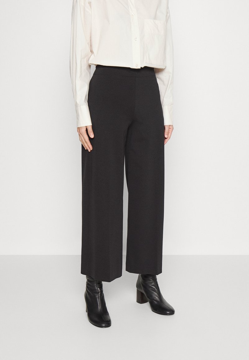 Zwarte wijde broek in een gladde stof, met een hoge taille en een getailleerde pasvorm, gecombineerd met zwarte leren enkellaarsjes met hak.