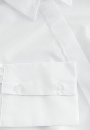 Chemise blanche avec une texture lisse, dotée d'un col classique et de poignets. Comprend deux boutons ronds et transparents sur le poignet pour la fermeture.