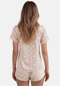 Beiger Baumwoll-Pyjama-Set mit einem kurzärmeligen Oberteil mit weißen Herzmustern und passender, locker sitzender Shorts. Weicher Stoff.
