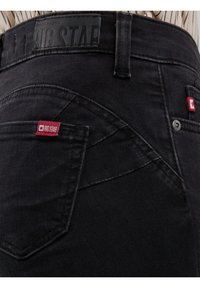 Prim-plan al buzunarului din spate al unei perechi de blugi negri, cu etichete roșii Big Star și o etichetă din piele neagră Big Star pe talie.