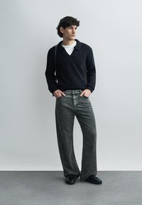 Black textured knit pullover and gray wide-leg jeans. Black shoes. Straight-cut silhouette with a v-neck and long sleeves.