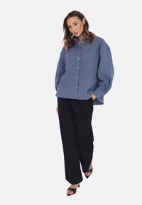 Niebieska koszula z guzikami, z dwiema kieszeniami na piersi, luźny krój i długie rękawy. Zestawiona z czarnymi, szerokimi spodniami z wysokim stanem i sandałami na obcasie z odkrytymi palcami.