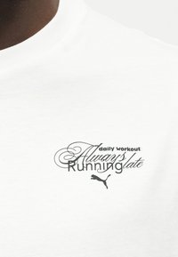 Κοντινή λήψη λευκού πουκαμίσου με μαύρο κείμενο "καθημερινή προπόνηση: Πάντα αργοπορημένος" και το λογότυπο της Puma κάτω από το κείμενο.