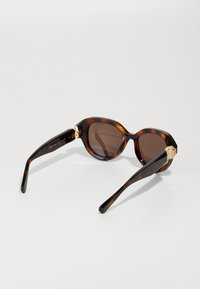 Braune Schildpatt-Sonnenbrille mit dunklen Gläsern, runder Form, dickem Acetatgestell und goldfarbenen Akzentbeschlägen an den Scharnieren.