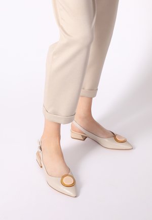 Beige leather slingback shoes with a pointed toe and a small block heel; features a circular beige accent at the front.