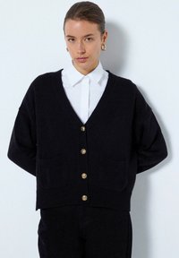 Mörk marinblå stickad cardigan med v-ringning, långa ärmar och två framfickor. Utrustad med fem guldtonade knappar för stängning.