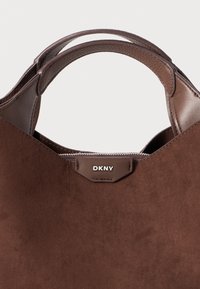 Brown suede tote bag with leather accents, dual handles, top zipper closure, and a DKNY logo tag on the front.