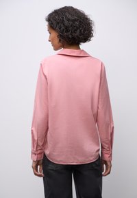 Lang gedragen shirt in zachtroze stof met een gladde textuur. Bevat een klassieke kraag en knoopmanchetten, gestyled met een ontspannen silhouet.