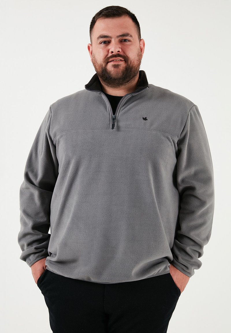 Grå fleece pullover med halv lynlås, der har en sort krave og et lille logo på brystet. Blød tekstur og afslappet pasform.
