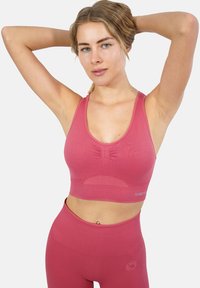Reggiseno sportivo rosa a coste con una fascia larga, scollatura a barca e arricciature sottili al centro. Abbinato a leggings a vita alta coordinati.