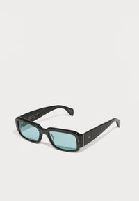 Gafas de sol rectangulares negras con lentes verdes. Hechas de plástico suave, presentan una sutil marca en las patillas y acentos metálicos.