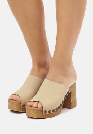 Sandali open-toe beige con tomaia in pelle liscia, tacco alto a blocco e hardware circolare decorativo lungo il lato.