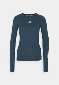 Långärmad atletisk tröja i mörk teal, tillverkad av fuktavvisande material. Har rundad halsringning och vitt logotyp på bröstet och ärmarna.