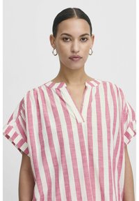 Tunika a strisce, a maniche corte, in rosa e crema; presenta un scollo a V parziale e un tessuto morbido e testurizzato con vestibilità rilassata.