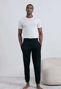 Biele tričko s okrúhlym výstrihom a malým červeným logom "HUGO", v kombinácii s čiernymi teplákmi s červeným detailom a nastaviteľným šnúrkou v páse.