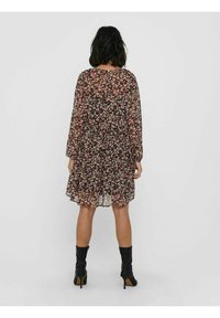 Robe noire à fleurs avec manches longues, matériau transparent, longueur au genou, ornée de petites fleurs roses et blanches, et un ourlet fluide.