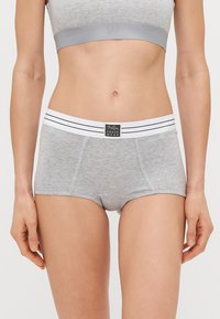 Γκρίζες βαμβακερές σορτς με φαρδιά λευκή ζώνη που διαθέτει δύο μαύρες ρίγες. Η ζώνη έχει μια μαύρη ετικέτα που γράφει "UNDER WEAR."