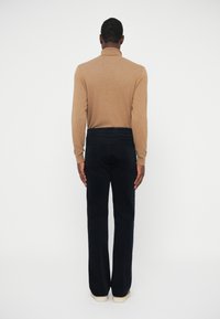 Brūns garām piedurknēm krekls apvienots ar tumši zilām platām biksēm. Apģērbs izceļas ar gludu tekstūru un precīzu piegriezumu, ar tonāla šuvuma redzamību.