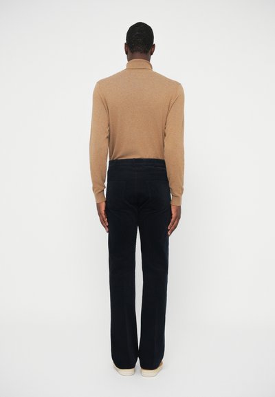 Braunes langärmliges Hemd kombiniert mit dunkelblauen Schlaghosen. Das Outfit zeigt eine glatte Textur und eine maßgeschneiderte Passform, mit sichtbaren tonalen Nähten.