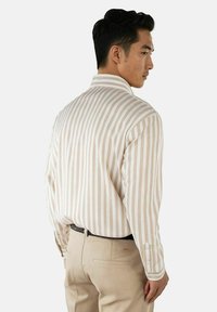 Lys beige stripete langermet skjorte med klassisk krage. Bakdelen har vertikale striper og en avslappet passform. Bært sammen med beige bukser.