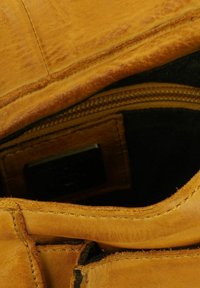 Interno di un portafoglio in pelle marrone con una texture liscia, dotato di un compartimento con cerniera e di un piccolo etichetta nera all'interno.
