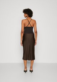 Camisole noir avec des bretelles croisées à l'arrière associé à une jupe midi en satin brun. Présente un corsage ajusté et une texture lisse et fluide.