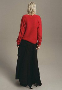 Pull en tricot rouge à coupe décontractée avec des poignets côtelés, associé à une longue jupe noire au design fluide.