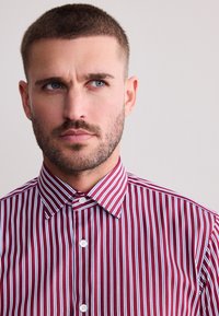 Rot-blau gestreiftes Hemd mit Knöpfen und klassischem Kragen. Hergestellt aus glattem Stoff mit normaler Passform und weißen Knöpfen vorne.