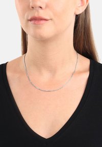 Collana in argento con un design delicato e texturizzato, posata sul collo, abbinata a una maglietta nera a scollo a V.