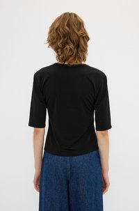 Sort kortærmet top med rund halsudskæring, tætsiddende ved skuldrene og løs i bunden, parret med brede denimbukser.