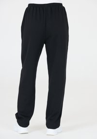 Zwarte sweatpants met een elastische tailleband en rechte pijpen, gemaakt van zachte stof. Gecombineerd met witte sportschoenen.