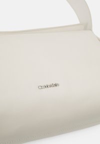 Borsa a tracolla in pelle color crema con una texture liscia e logo Calvin Klein argentato. Presenta un design elegante e cuciture minimaliste.