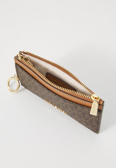 Portefeuille marron monogrammé avec des accents beiges, fermeture éclair dorée et porte-clés. Ouvert, révélant un intérieur beige et une étiquette de marque à l'intérieur.