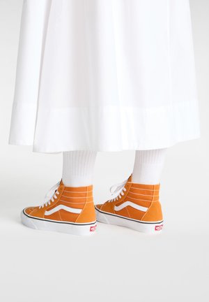 Zapatillas altas de ante naranja con acentos blancos, que presentan un diseño de cordones y una suela en contraste negra y blanca. Medias blancas de canalé visibles.