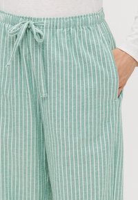 Pantaloni a righe verde chiaro con una consistenza morbida, dotati di vita regolabile con coulisse e tasche laterali, progettati con strisce bianche alternate.