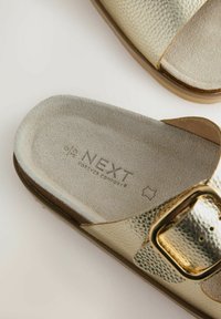 Mule en cuir doré avec boucle ajustable et semelle intérieure en daim étiquetée "NEXT Forever Comfort" taille 6/39 sur un fond clair.