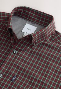 Camicia a quadri rossa e verde con bottoni e collo classico, caratterizzata da una trama tessuta e una piccola etichetta del marchio sulla patta dei bottoni.