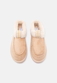 Tan suede slip-on shoes with a fluffy cream collar, decorative stitching, and a woven accent band. Soft texture and rounded shape.