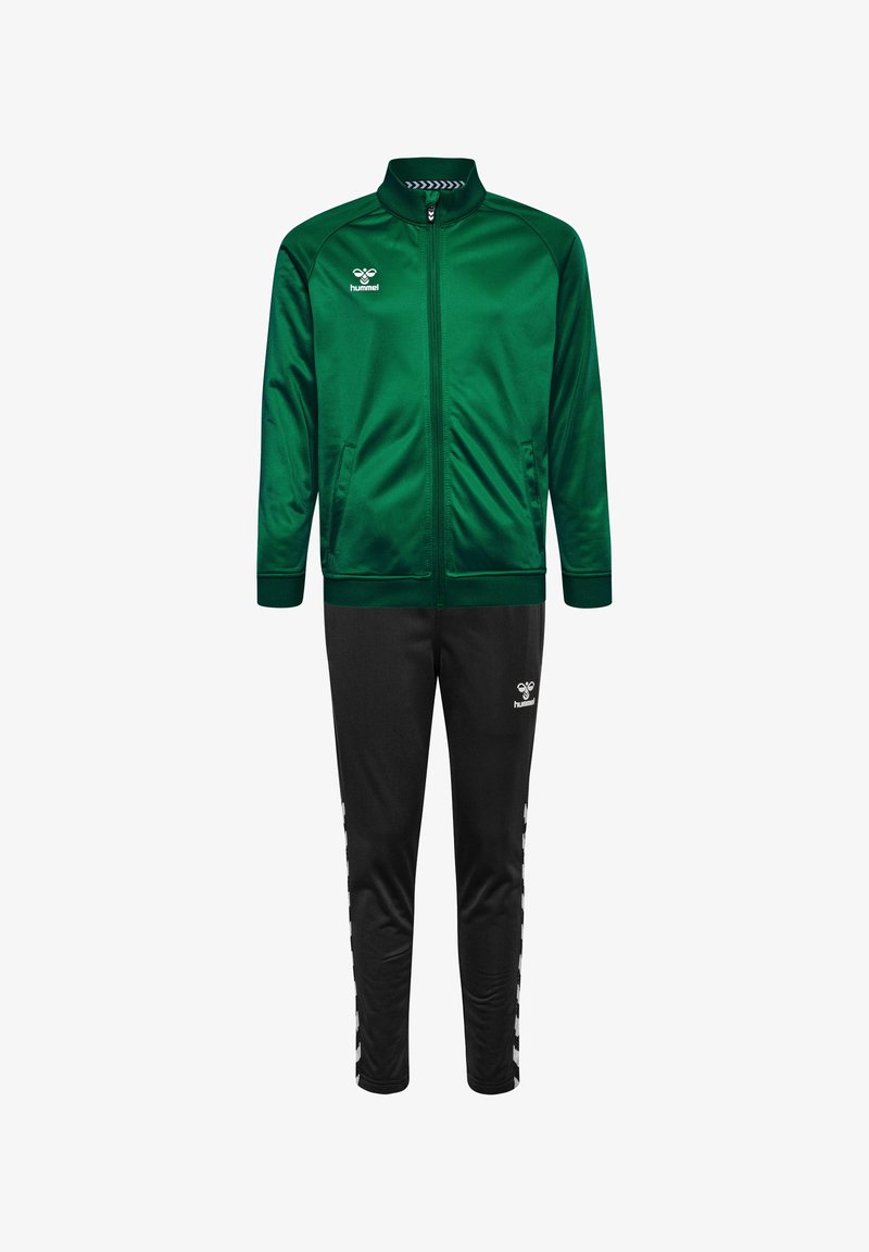Zielona satynowa kurtka sportowa z wysokim kołnierzem, zapinana na zamek błyskawiczny, z bocznymi kieszeniami, w połączeniu z czarnymi spodniami z białymi akcentami i logo.